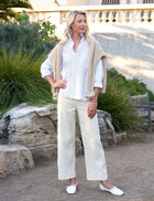 Woman in a white shirt and beige pants standing in front of a building with greenery.