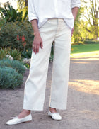 Person wearing a white shirt and light-colored pants standing outdoors with greenery in the background