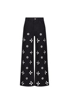 The Kaia Pearl High Rise Jean in black features wide-leg denim with white daisy cutouts on the front, finished with a button and zip waist closure.