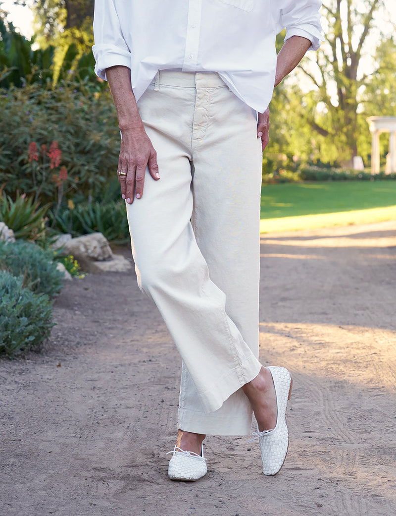 Person wearing a white shirt and beige pants standing outdoors on a path.