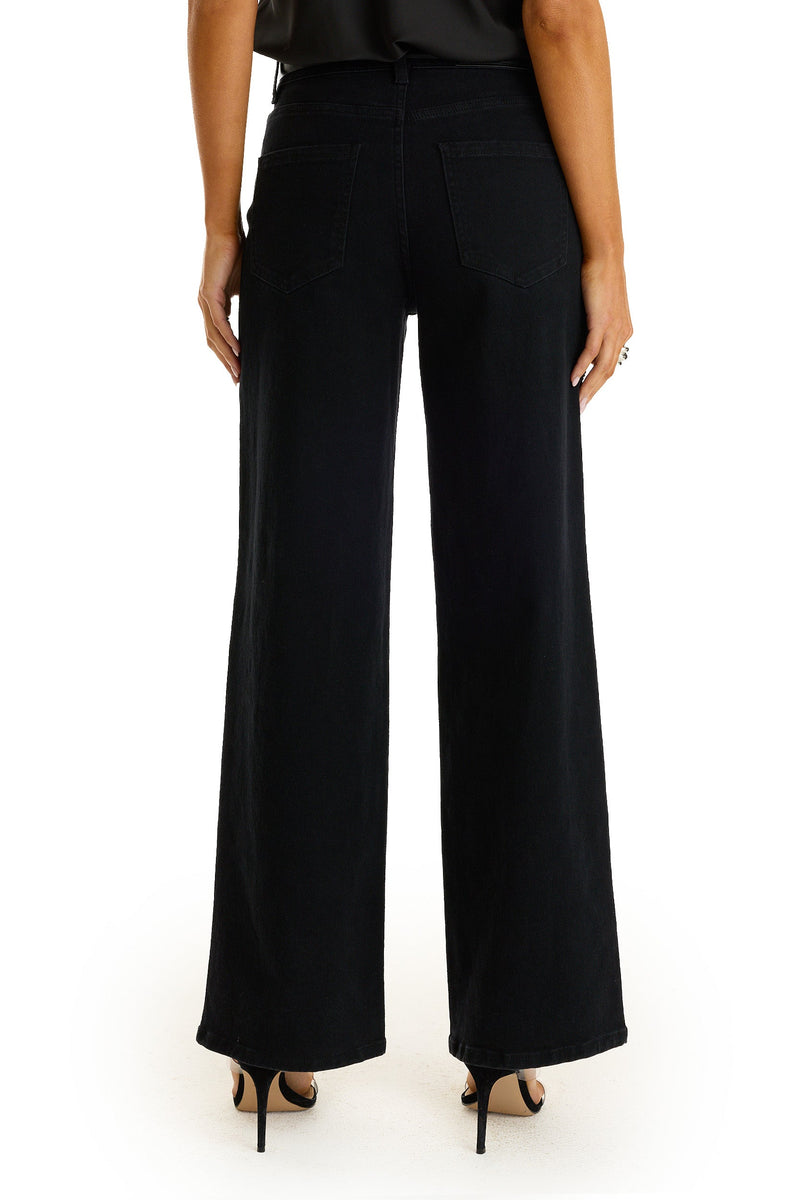 A person is shown from the back, standing against a white background, wearing the Kaia Pearl High Rise Jean in black and black high-heeled sandals.